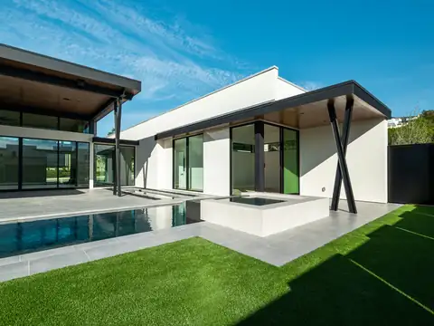 Backyard with bright green artificial turf lawn bordered by large gray concrete pavers, pool, and modern house