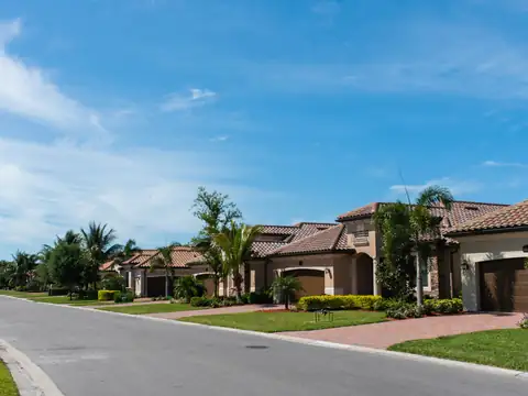 Sunny street of Mediterranean-style Florida homes with paver driveways, palm trees, and manicured lawns