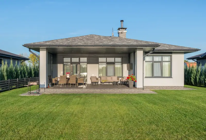 House exterior with a large manicured green lawn, covered patio, and outdoor seating area