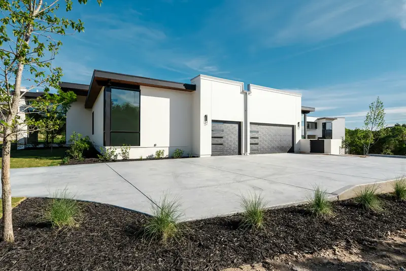 Large smooth concrete driveway in front of a modern white house with two dark garage doors
